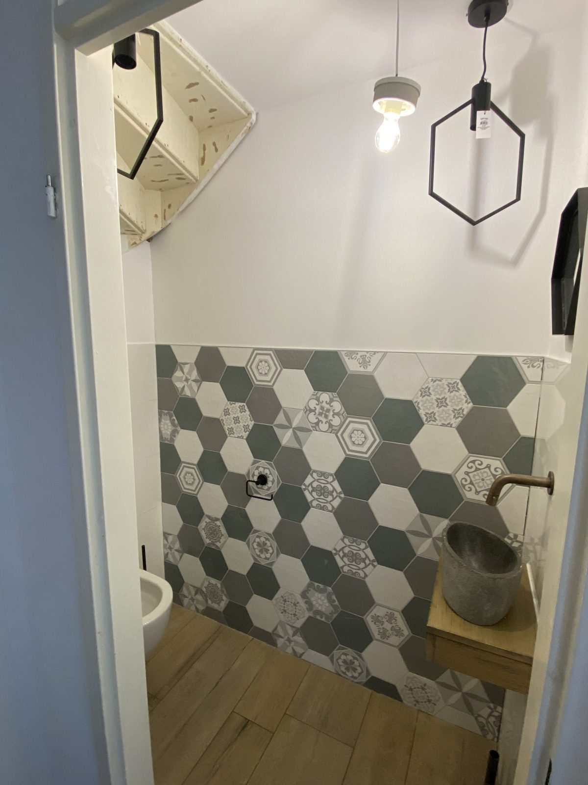 Toilet met grijs-witte zeshoekige patroontegels, stenen waskom en houtlook vloer