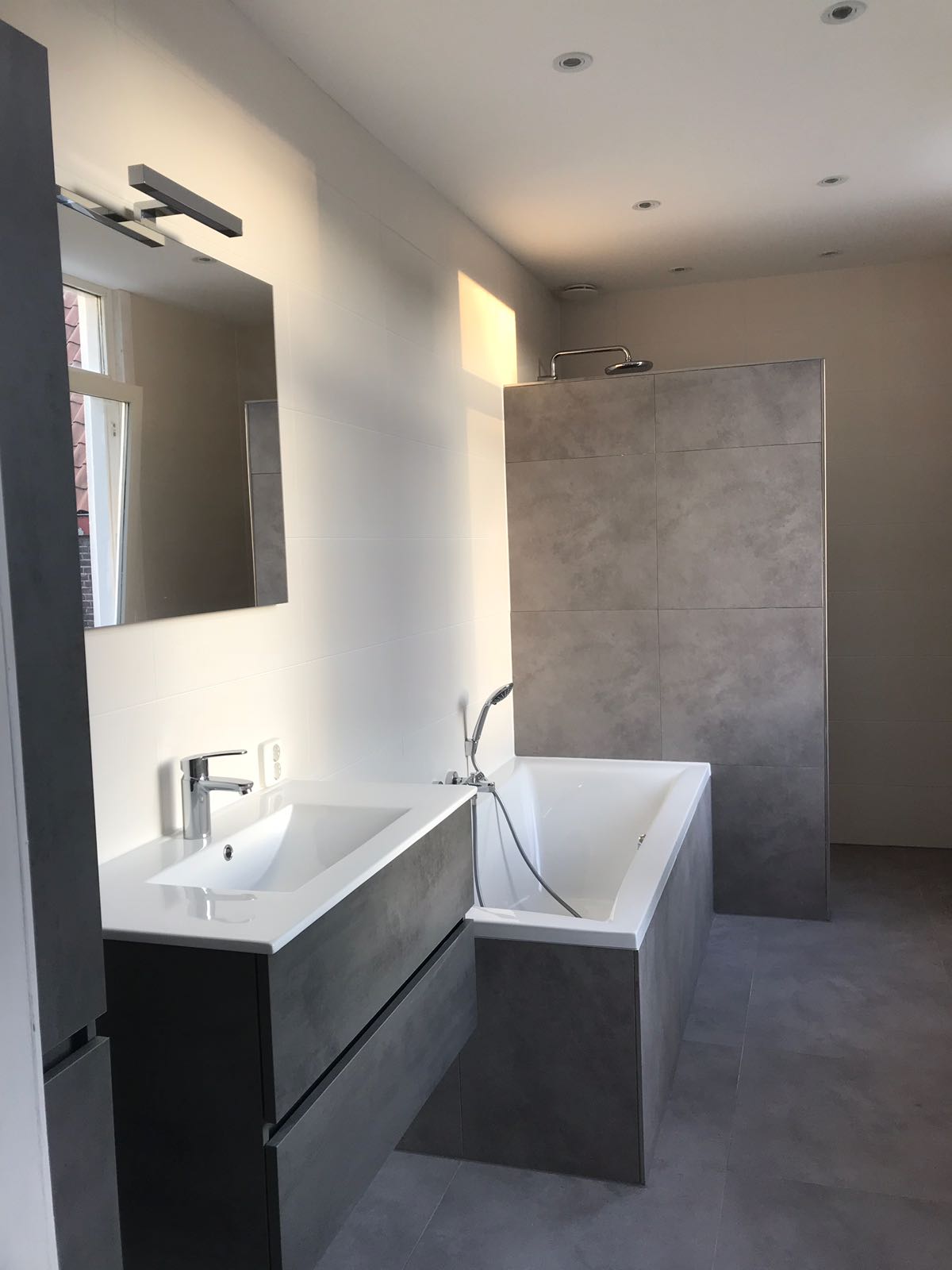 Badkamer met betonlook tegels, bad en badmeubel met spiegelverlichting
